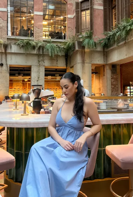 Modelo sentada em um café com vestido longo azul de alças